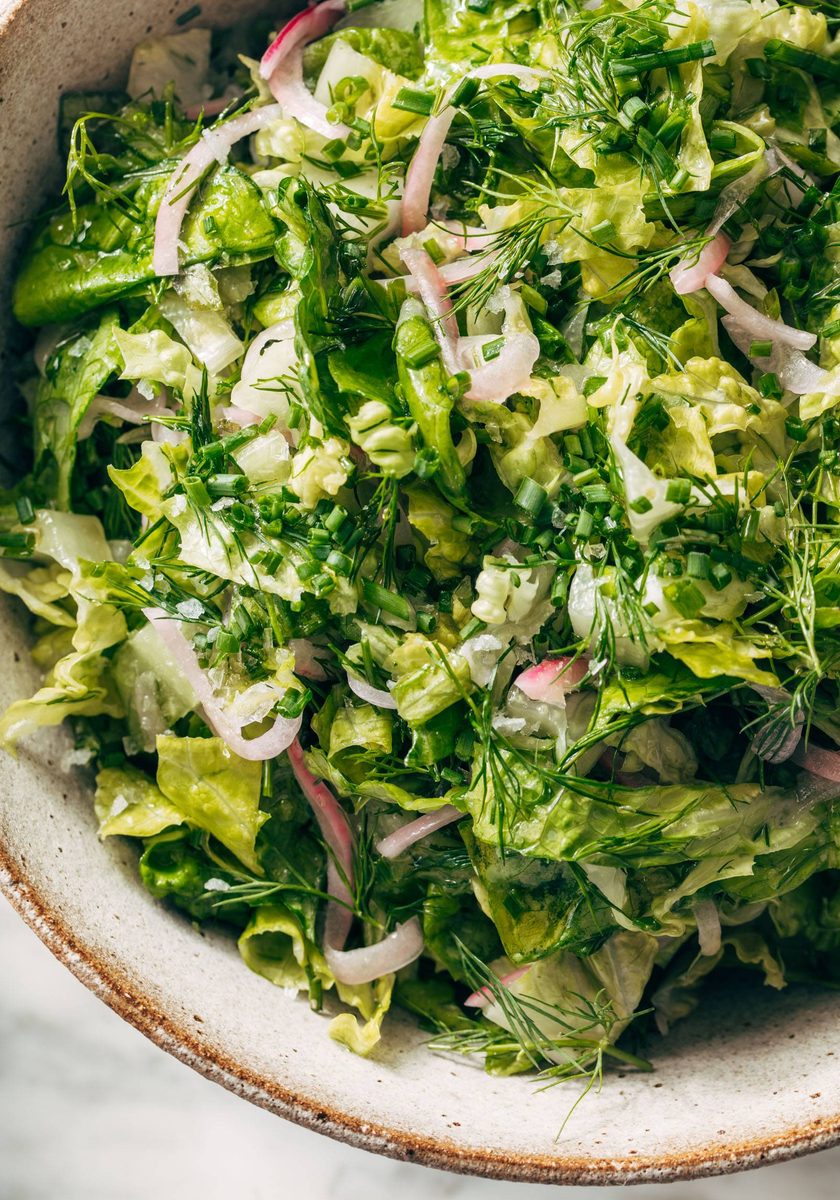 Salad with lettuce, fresh herbs, and pickled onions in a bowl.
