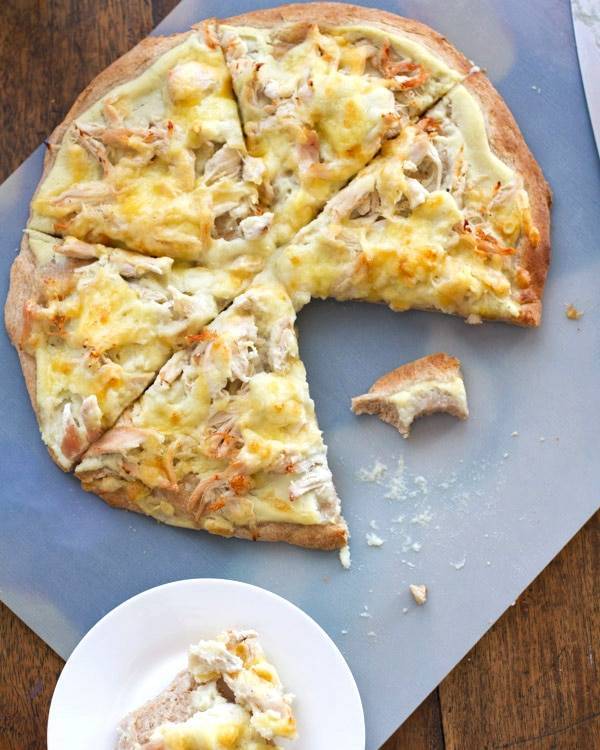 Chicken Alfredo pizza slices on a white surface.