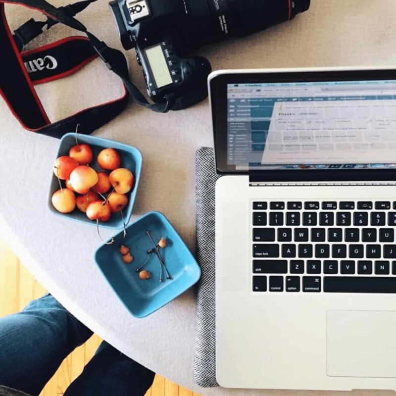 A laptop sitting on a table with fresh cherries.