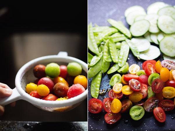 Tomatoes in a strainer and veggies on a black surface.