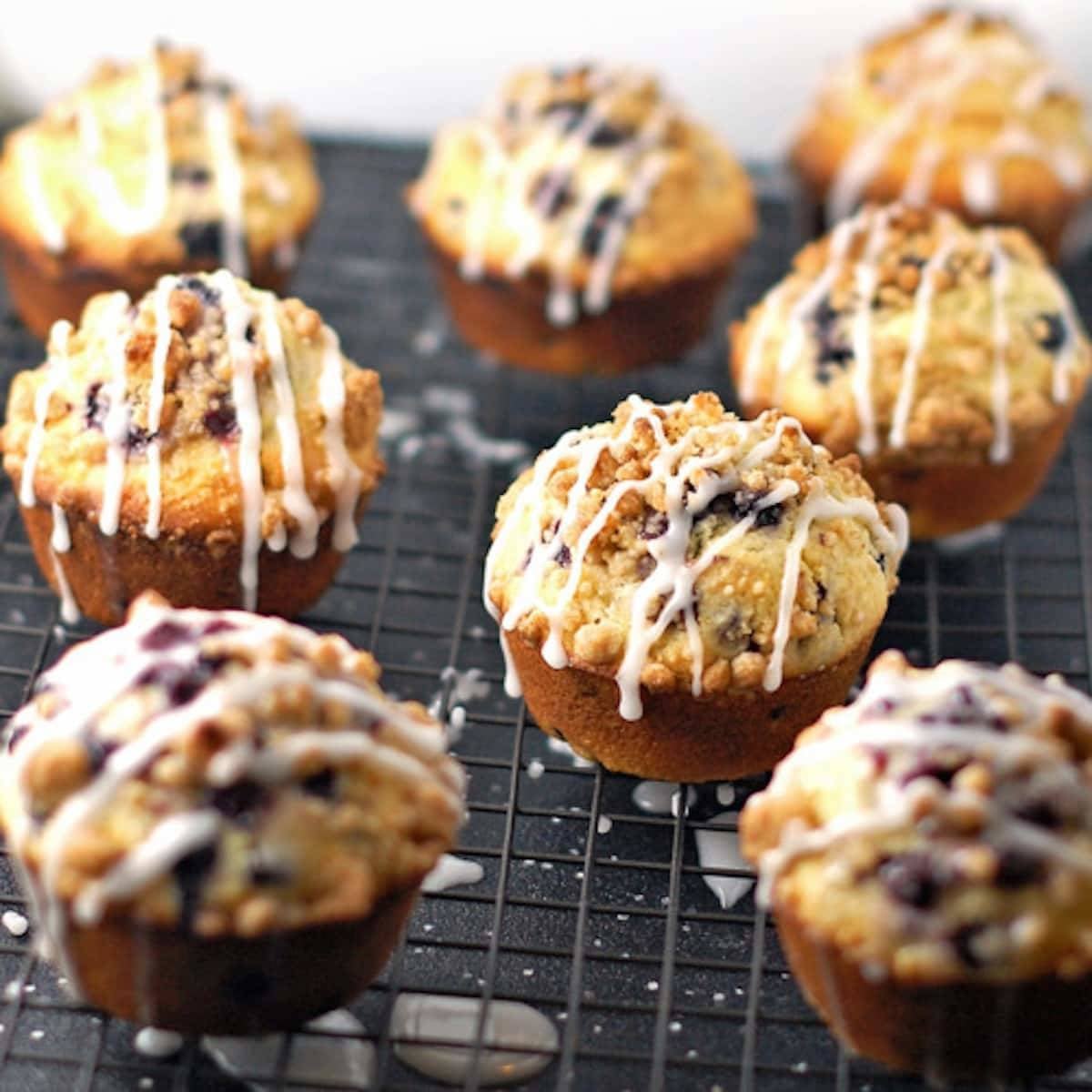 Cornmeal blueberry muffins topped with streusel and glaze on a drying rack.