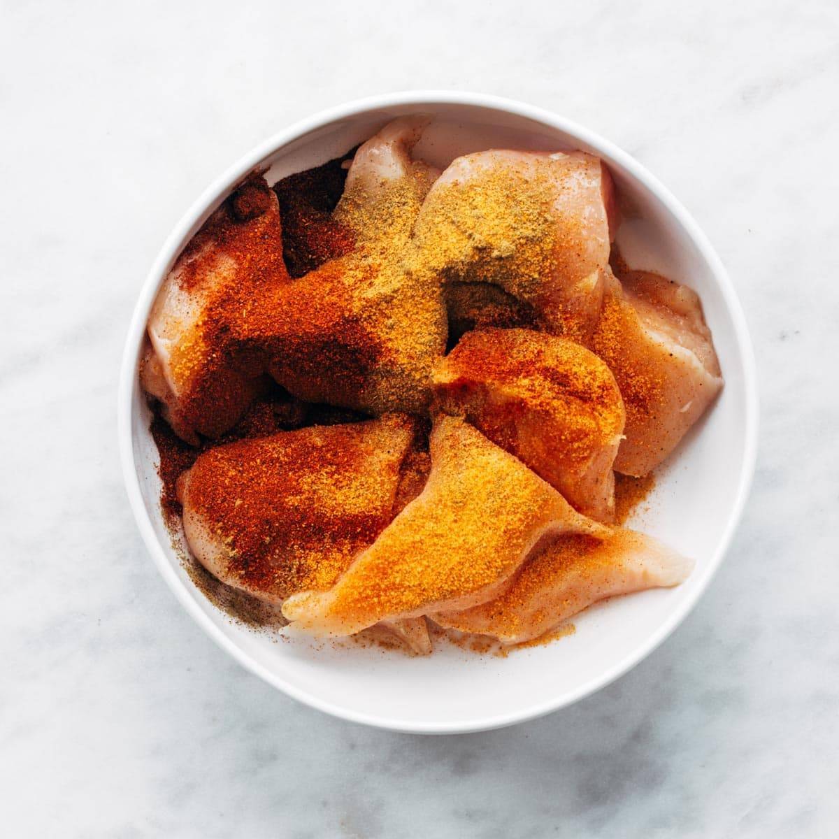 Seasoned chicken breasts in a bowl.